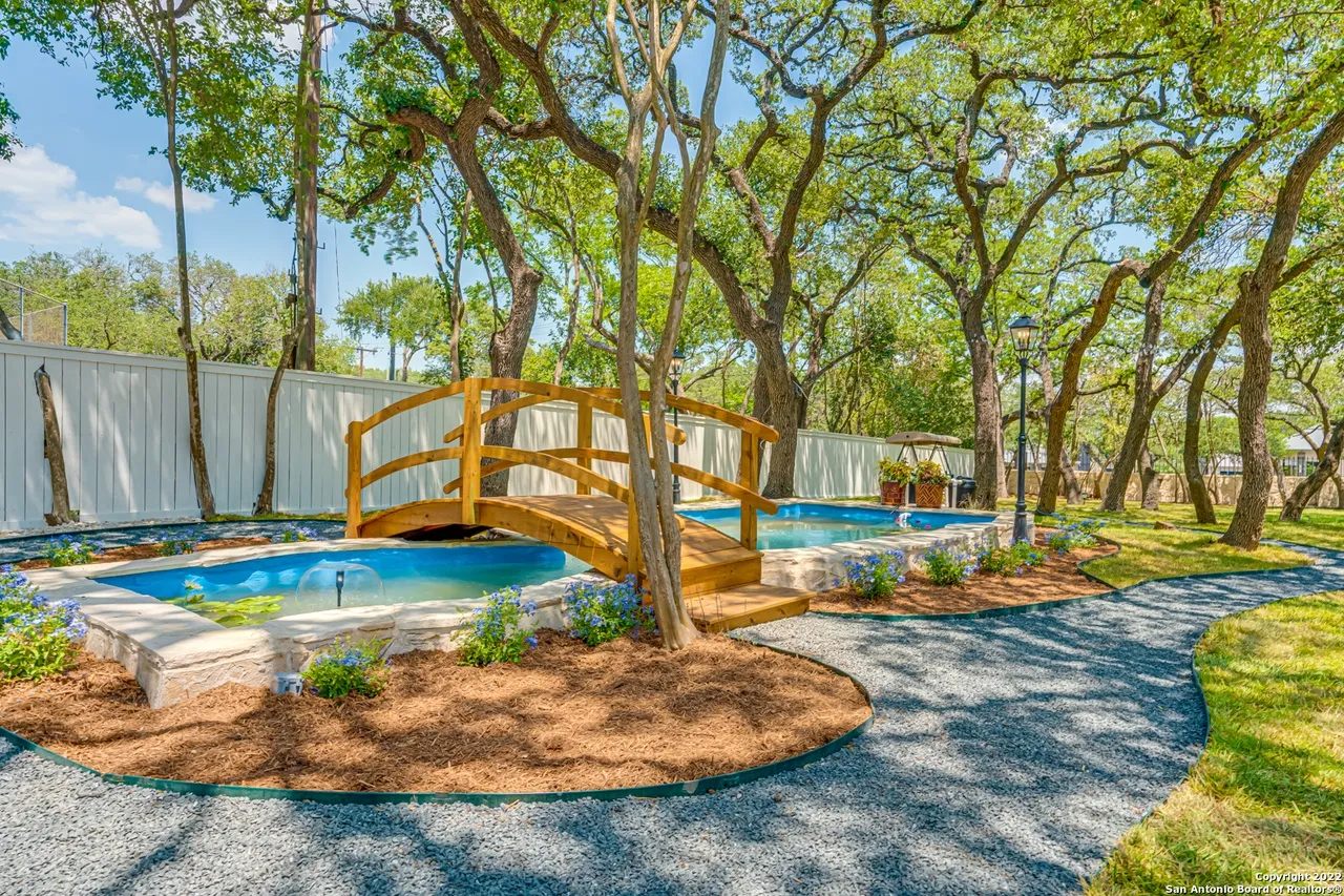 Castle Hills backyard remodel with custom koi pond, wooden arched bridge, stone edging, and mature oak trees in San Antonio TX