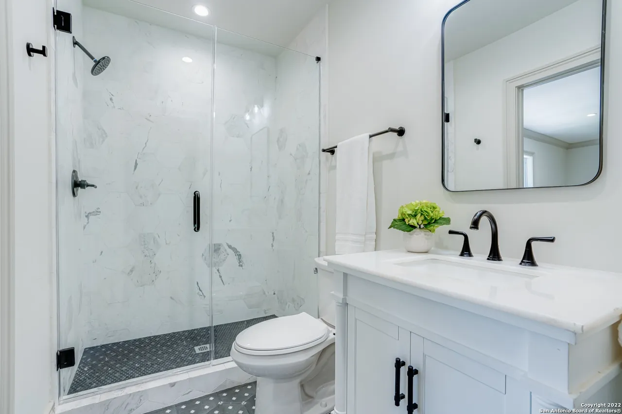 Frameless glass shower remodel with large-format marble hexagon tile and matte black fixtures in Castle Hills San Antonio TX