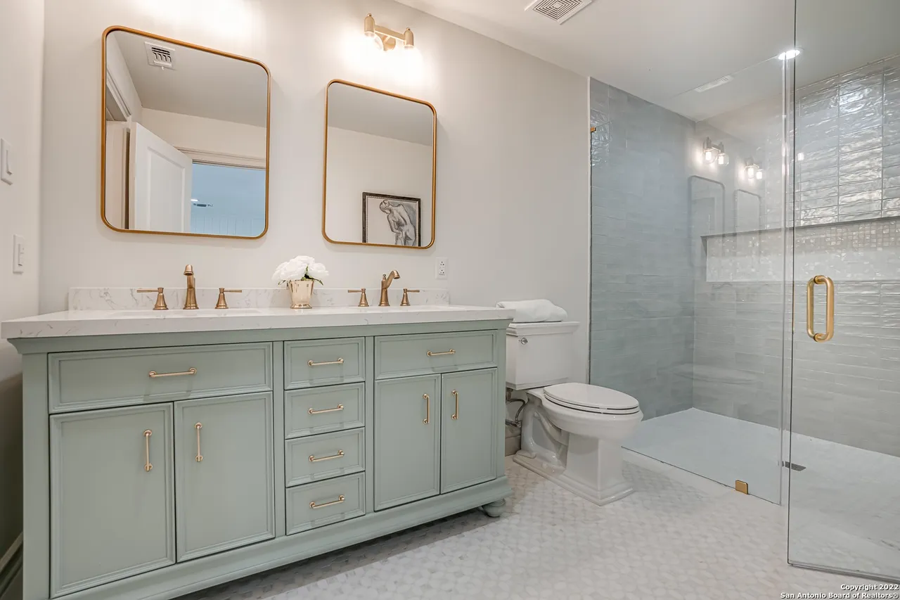 Bathroom remodel with mint green double vanity, gold hardware, frameless glass shower, and marble mosaic floor in Castle Hills San Antonio TX