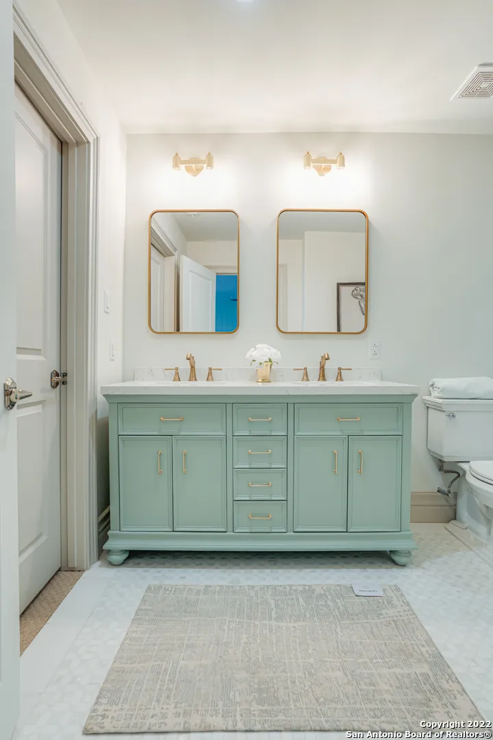 Bathroom remodel with sage green double vanity, gold hardware, dual gold-framed mirrors, and marble mosaic floor in Castle Hills San Antonio TX