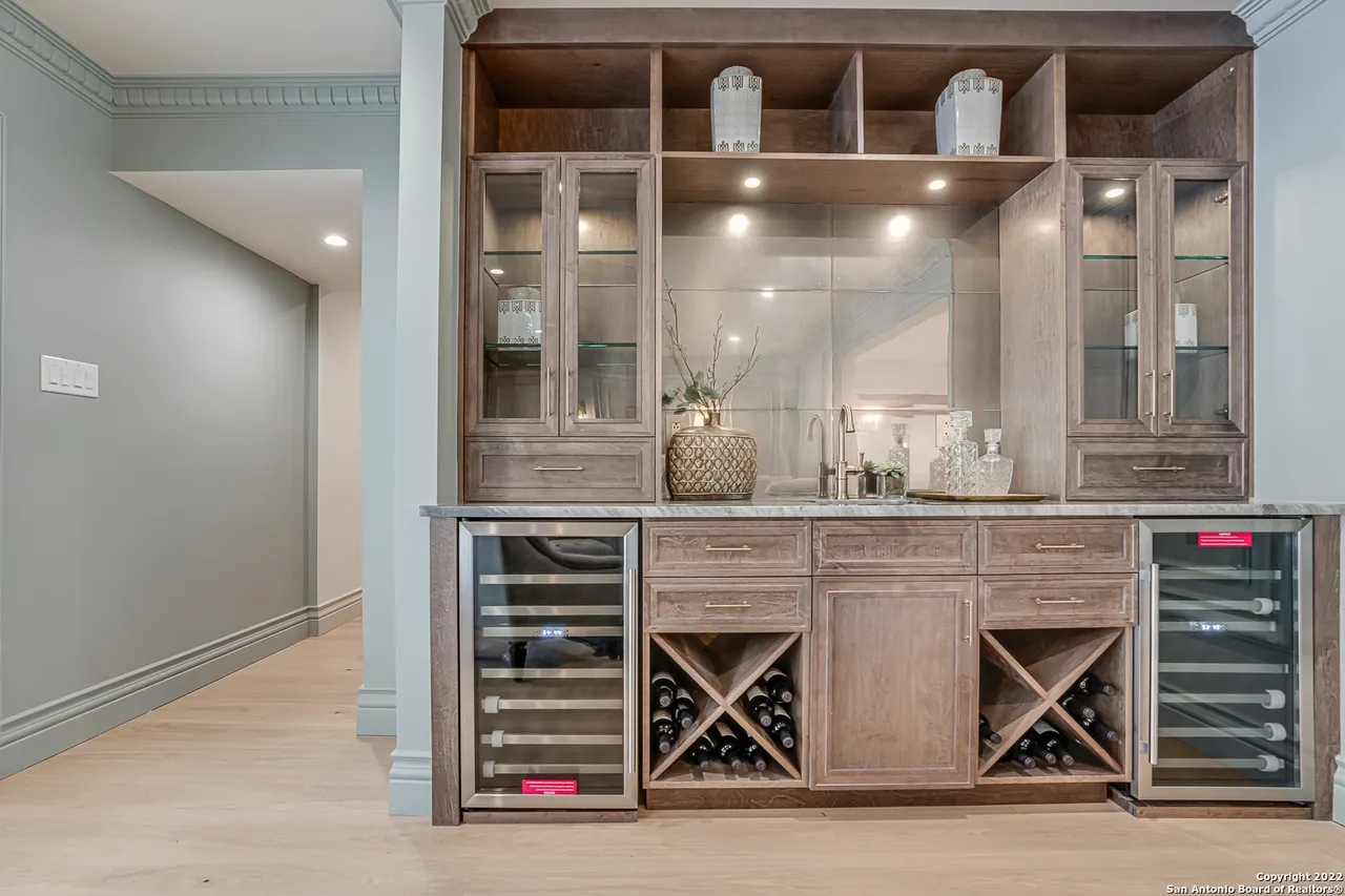 Custom wet bar remodel with built-in wine storage, dual wine coolers, glass-front cabinets, and marble countertop in Castle Hills San Antonio TX