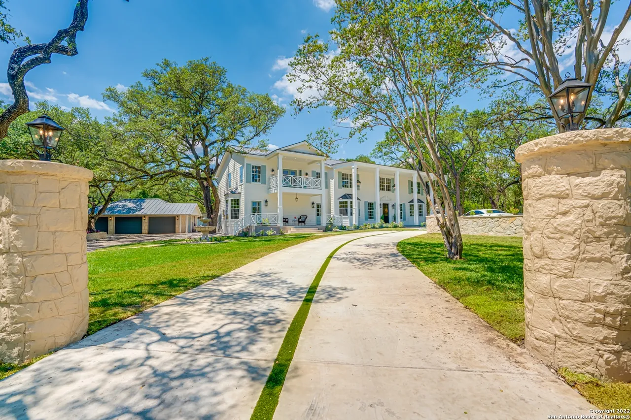 Castle Hills estate front entrance remodel with limestone pillar gate, gas lanterns, curved concrete driveway, and wraparound porch in San Antonio TX