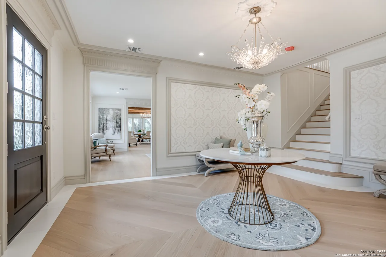 Remodeled grand foyer with crystal chandelier, herringbone hardwood floors, and decorative wallpaper accent wall in Castle Hills San Antonio TX
