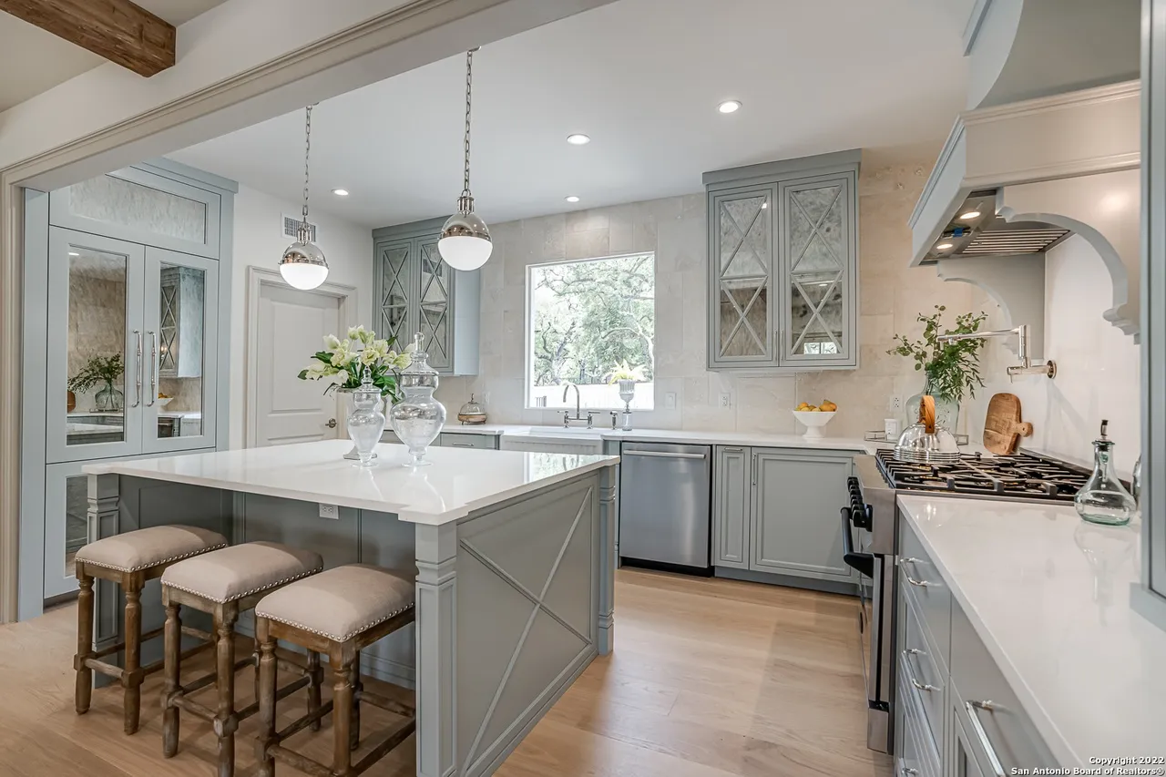 Castle Hills kitchen remodel with quartz island barstools, mirrored pantry door, and custom sage cabinetry in San Antonio TX