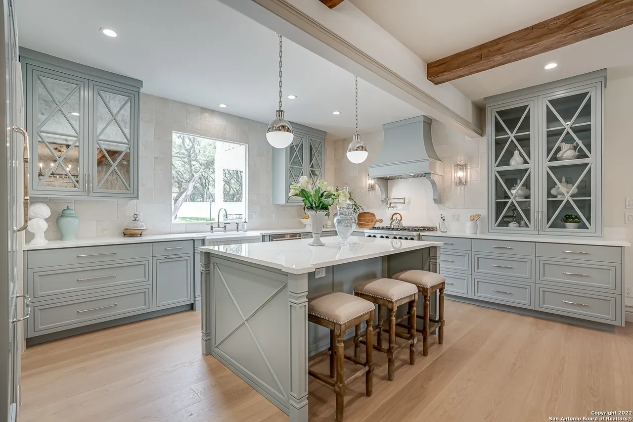 Remodeled kitchen with sage blue-gray cabinetry, quartz island, pendant lights, and reclaimed wood beams in Castle Hills San Antonio TX