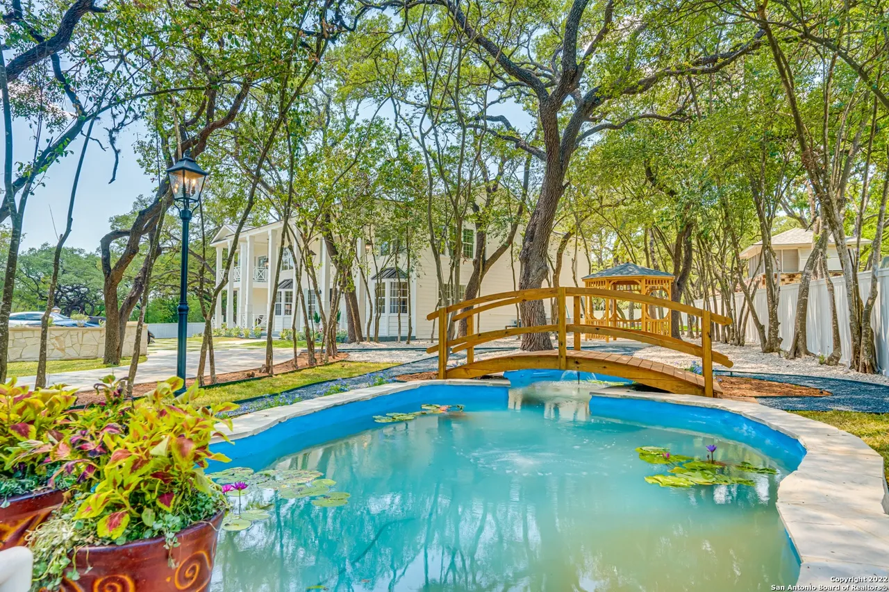 Castle Hills estate koi pond remodel with lily pads, wooden arched bridge, gazebo, and gas lantern posts in San Antonio TX