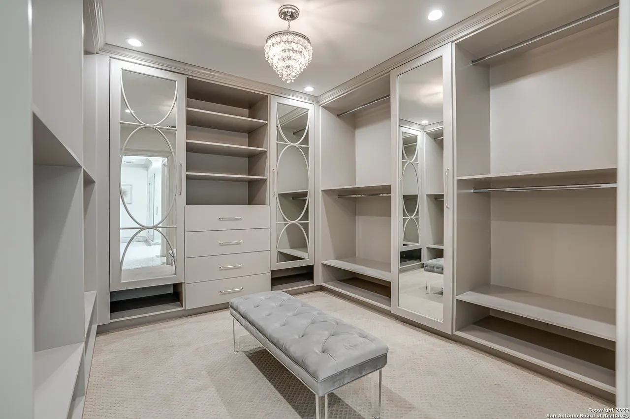 Luxury primary walk-in closet remodel with custom mirrored cabinet doors, crystal chandelier, and tufted velvet bench in Castle Hills San Antonio TX