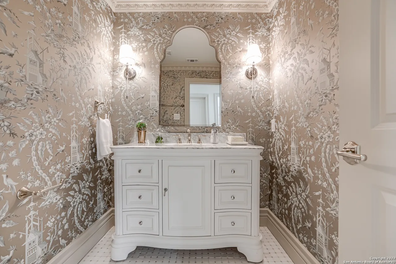 Elegant powder bath remodel with floor-to-ceiling chinoiserie wallpaper, white marble vanity, and arched mirror in Castle Hills San Antonio TX