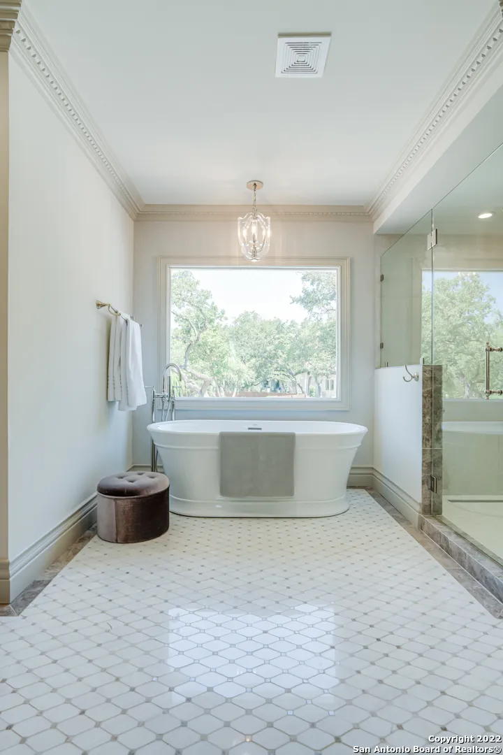 Primary spa bath remodel with freestanding soaking tub, large picture window, chandelier, and marble mosaic tile floor in Castle Hills San Antonio TX