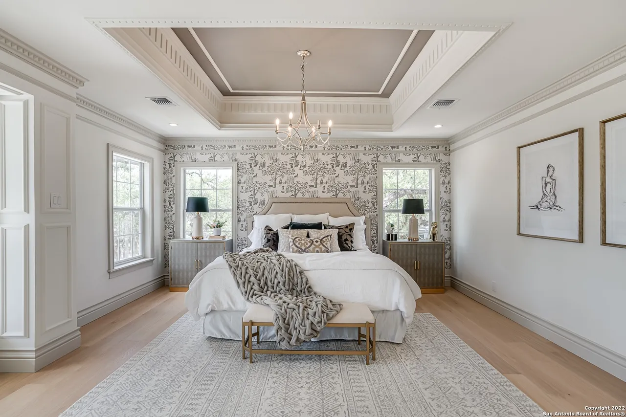 Luxury primary bedroom remodel with ornate tray ceiling, chandelier, toile wallpaper, and European white oak floors in Castle Hills San Antonio TX