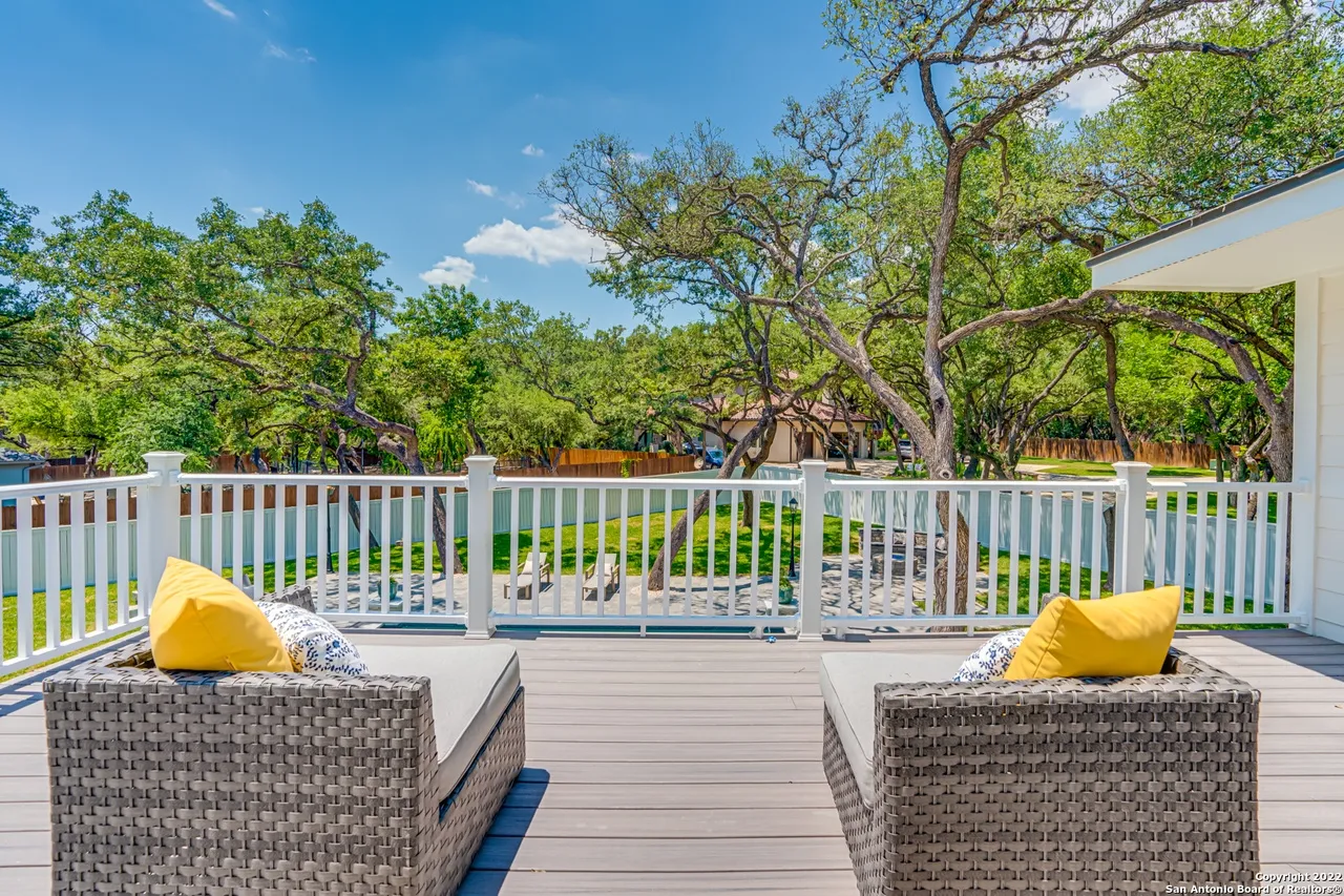 Second-story outdoor deck remodel with wicker lounge chairs, white balcony railing, and mature oak tree canopy at Castle Hills San Antonio TX