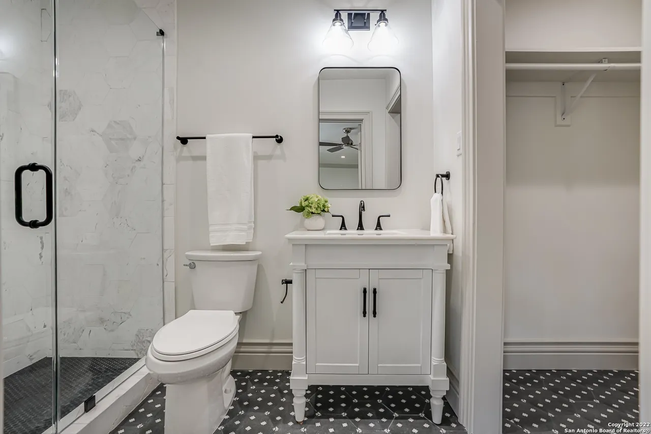 Secondary bathroom remodel with white vanity, matte black hardware, hexagon marble shower tile, and dark mosaic floor in Castle Hills San Antonio TX