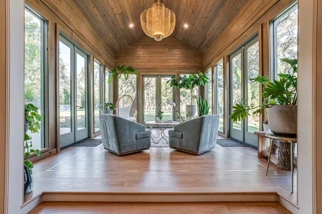 Completed sunroom renovation with vaulted wood ceiling, floor-to-ceiling windows, and modern lounge seating in San Antonio TX